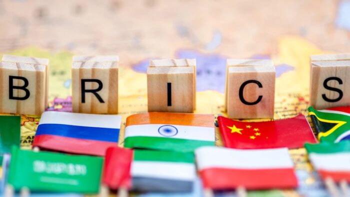 A Brics concept with letter tiles and small country flags on a world map background.