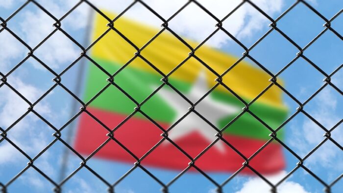 A steel mesh against the background of a blue sky and a flagpole with the flag of myanmar